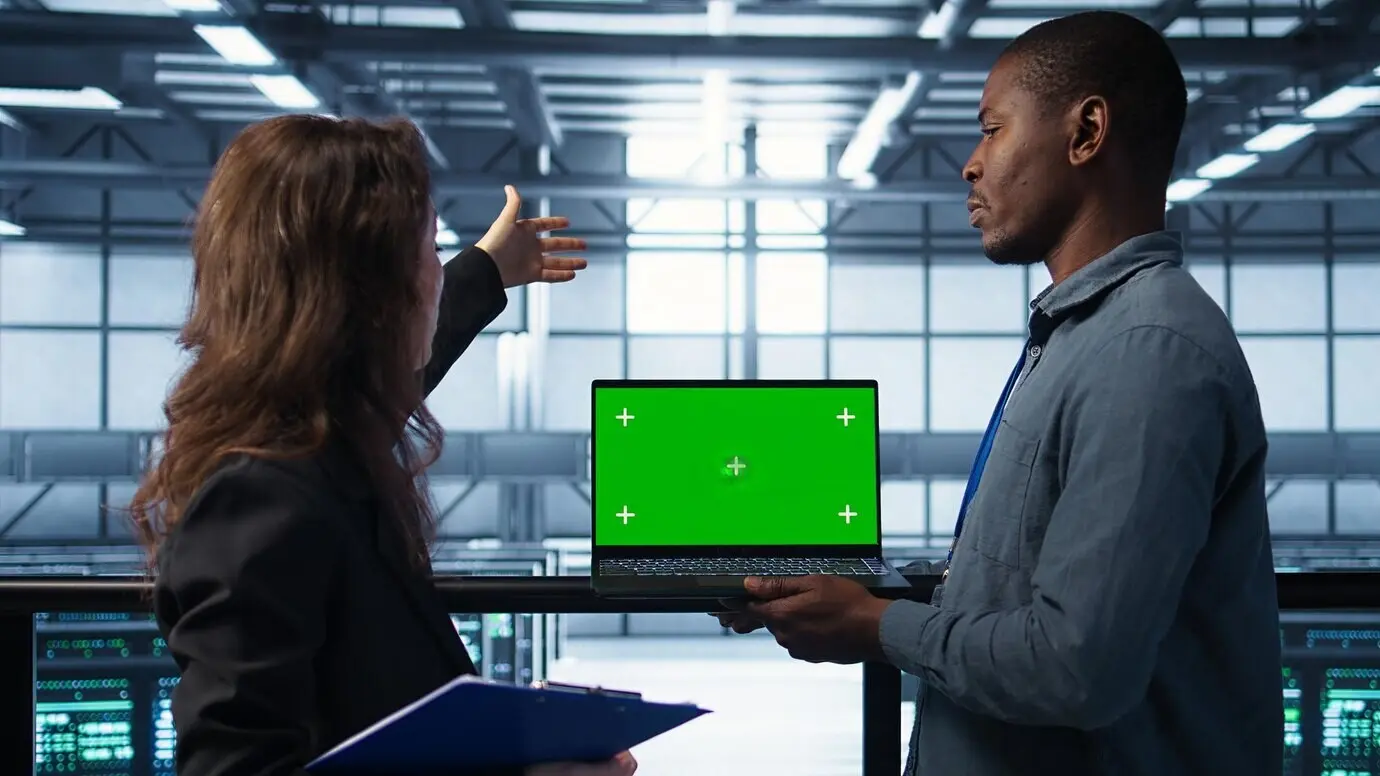 Ingenieros en un centro de datos, usando un portátil con pantalla verde, revisan la salud del equipamiento.